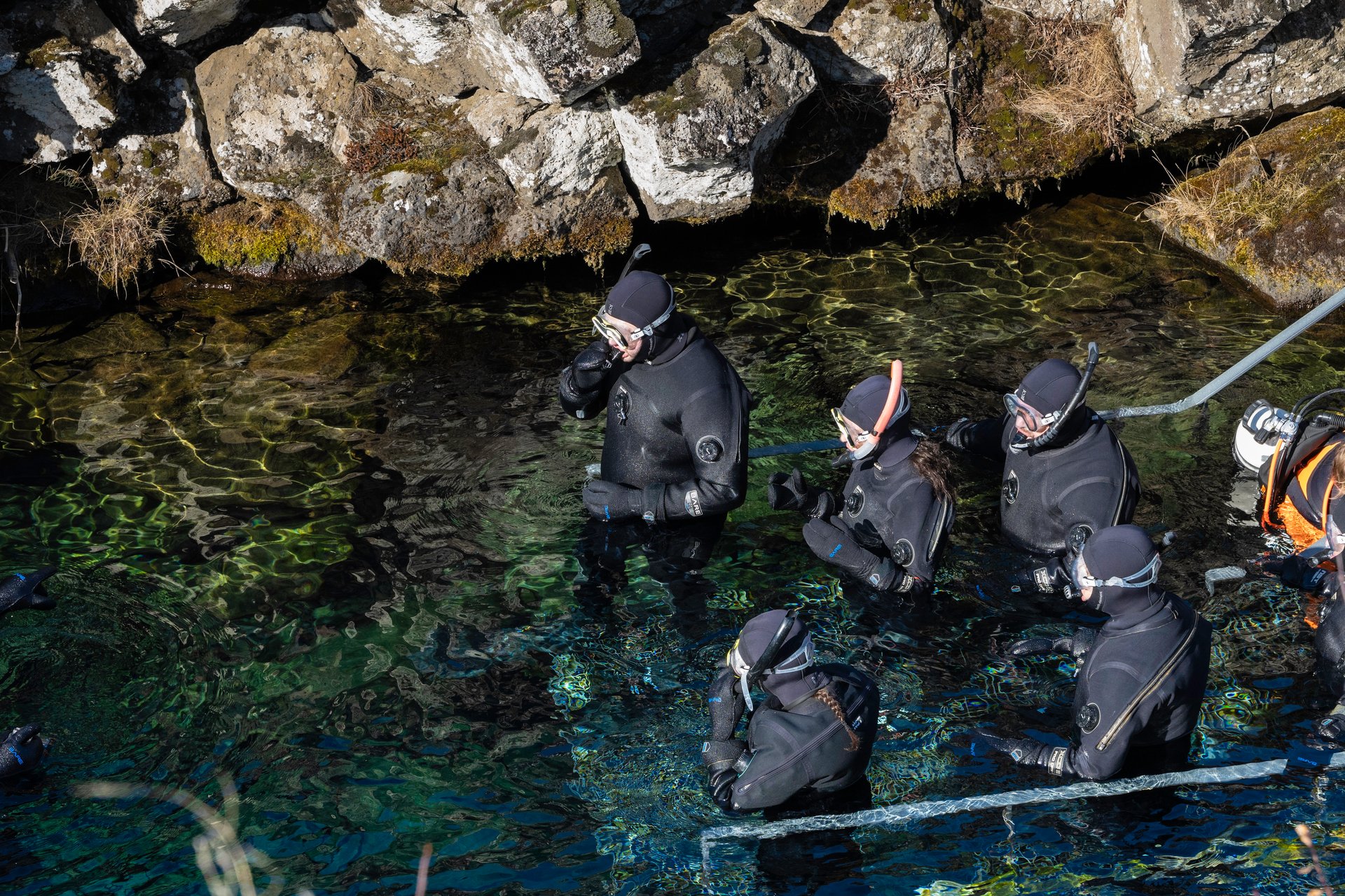 People in dry suit floating in the clear waters of Silfra