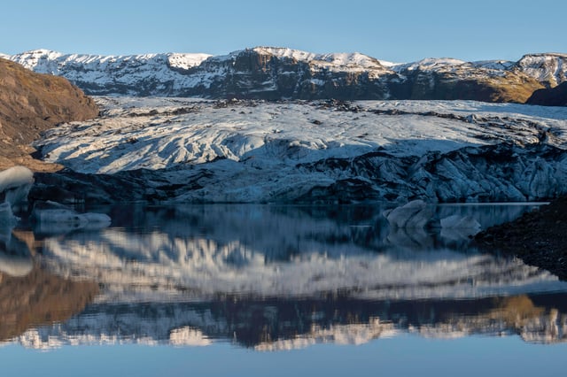 The mouth of the glacier Sólheimajökull is reflecting in the peaceful lake waters