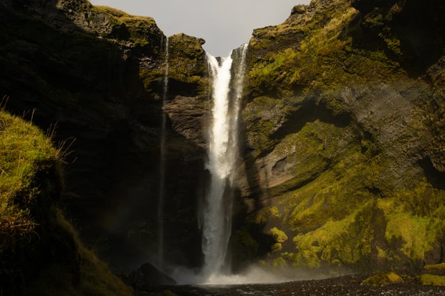 A thin, beautiful waterfall named Kvernufoss is nestled at the bottom of a green canyon