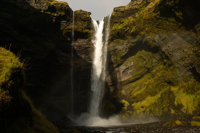 A green and dark canyon with the thin Kvernufoss waterfall flowing majestically