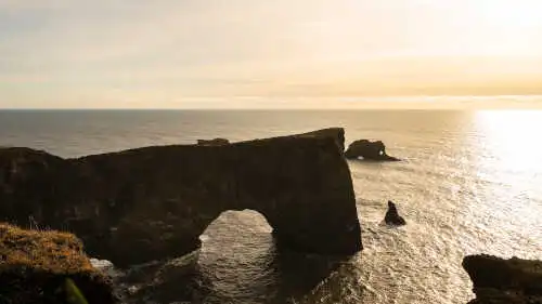 Une arche de pierre domine un ocean agité sous le lever du soleil