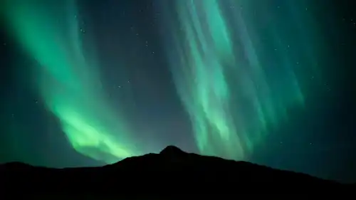 Des aurores boréales vertes dancent derrière une montagne