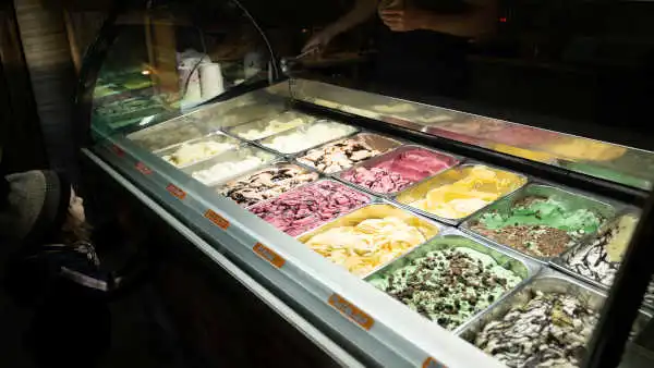 Une petite fille lorgne sur une vitrine pleine de glace de différentes couleurs