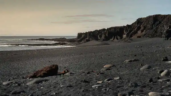 Black sand beach with rusty ship parts scattered around