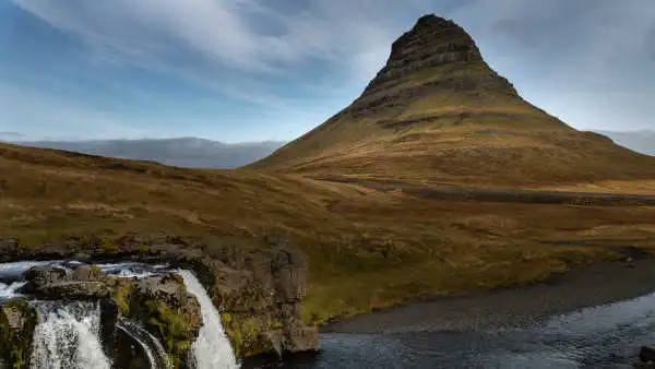 Green conic mountain behind two waterfalls