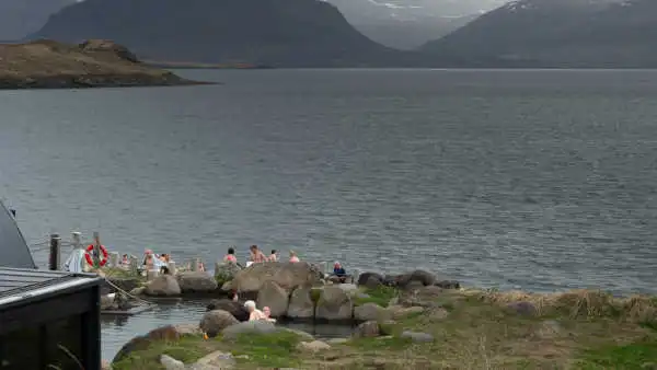 People bathing in a hot spring next to a fjord