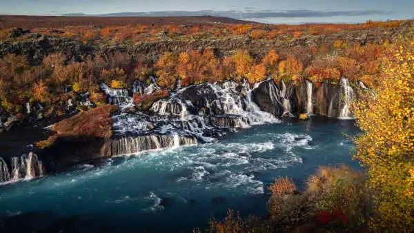 Among an autumnal landscape, a dozen of waterfalls are falling into a huge river