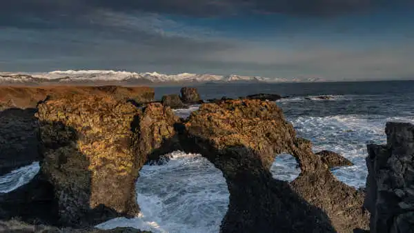 A stone arch is dominating the ocean at sunset