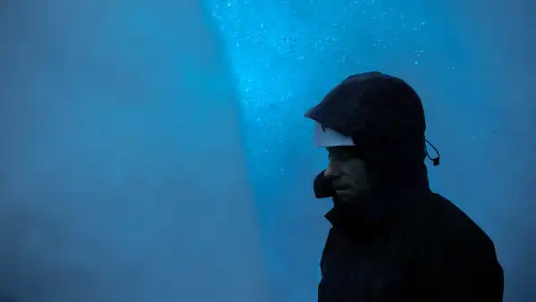 Someone is wearing a hood and helmet in a blue ice cave