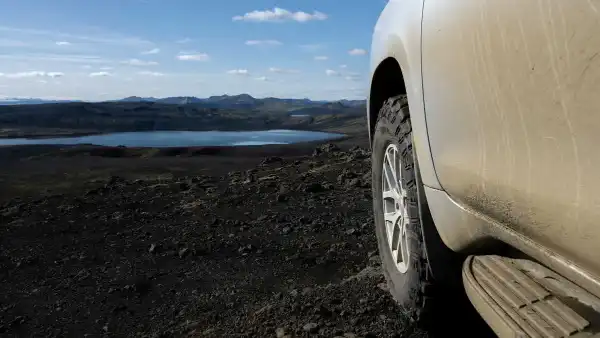 The dirty wheel of an offroad vehicle in photographed with lake and mountains in the background