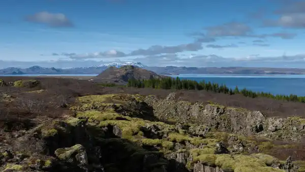 Moss covered tectonic fissure with mountains and lake in the background