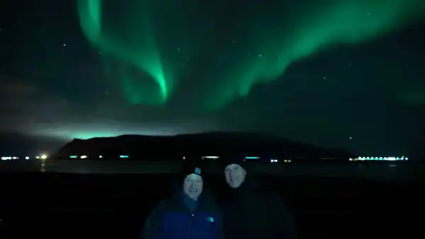 A couple is standing before the auroras borealis and are smiling