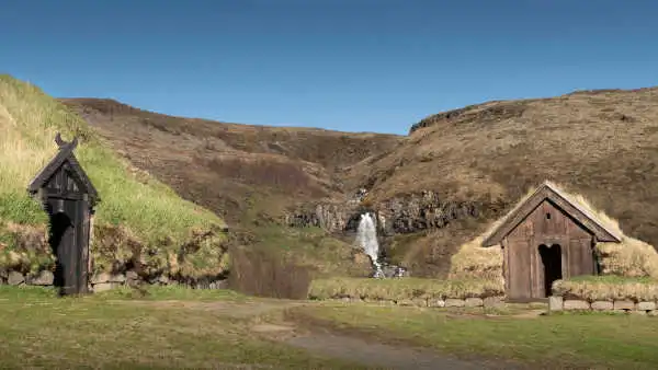 Two turf houses with a waterfall in the background