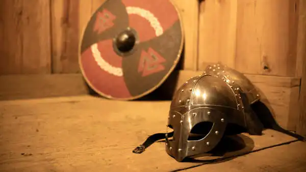 A viking helmet on a wooden board, with a shield in the background