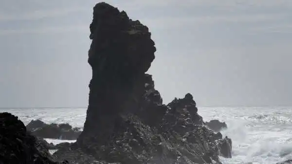 A huge rock is standing like a tower over an agitated ocean