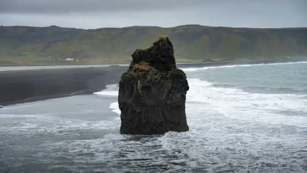 A huge rock standing alone on a black sand beach