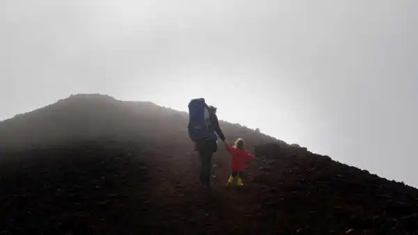 A mother and her kid are hiking to the top of a red volcano