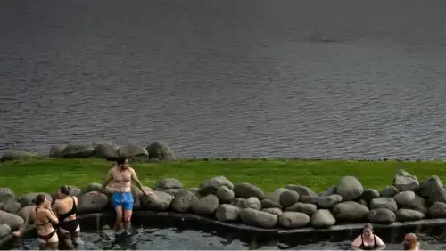 People are swimming in a hot pool, just by the side of a lake