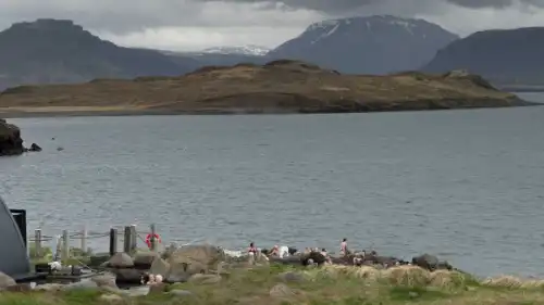 People are swimming in hot springs, located at the bottom of a fjord