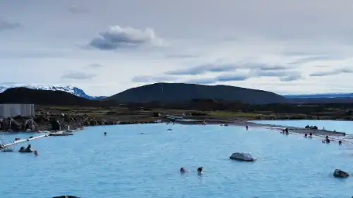 People are bathing in front of mountains in a huge pool, filled with milky-blue water