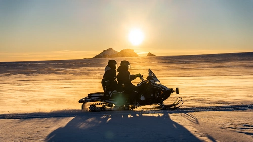 Snowmobilers racing across Langjökull glacier with mountain backdrop