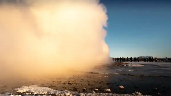 A crowd of people is standing next to an immense cloud of steam, that followed a geyser eruption