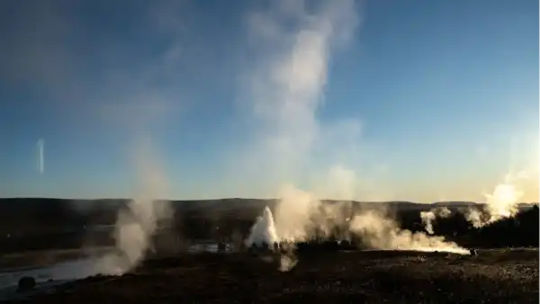 A geyser is blowing up, as seen from a distance, surrounded by steam clouds