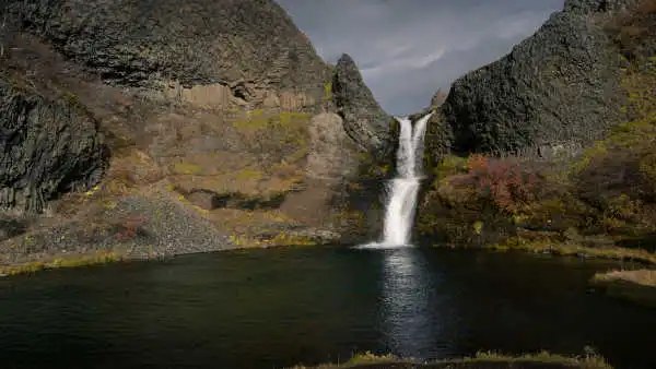 A beautiful waterfall falls among basaltic columns into a crystal clear lake