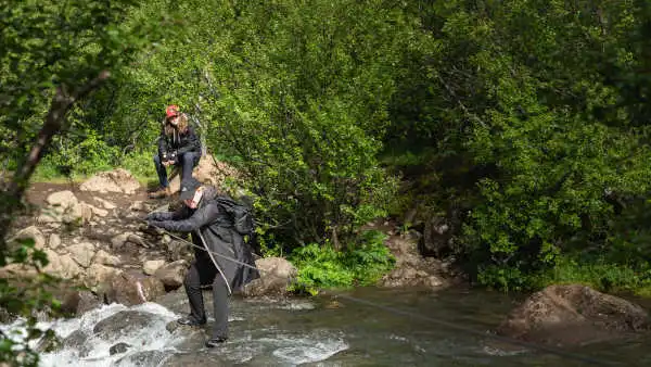 Two customers are crossing a river walking on a wooden log