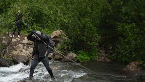 A client is passing under an iron wire, while walking on a wooden log over a river