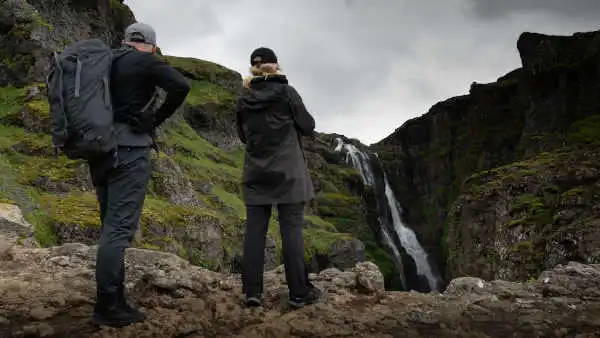 Two persons in the foreground are taking pictures of a tall waterfall