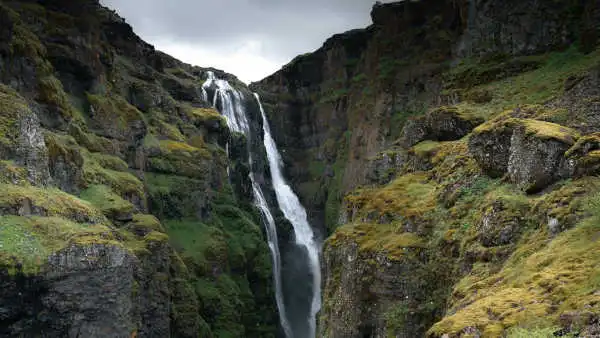 A tall, magnificent waterfall is falling inside of a canyon