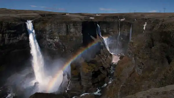 Two breathtaking waterfalls fall into a huge canyon, with rainbow shining over them