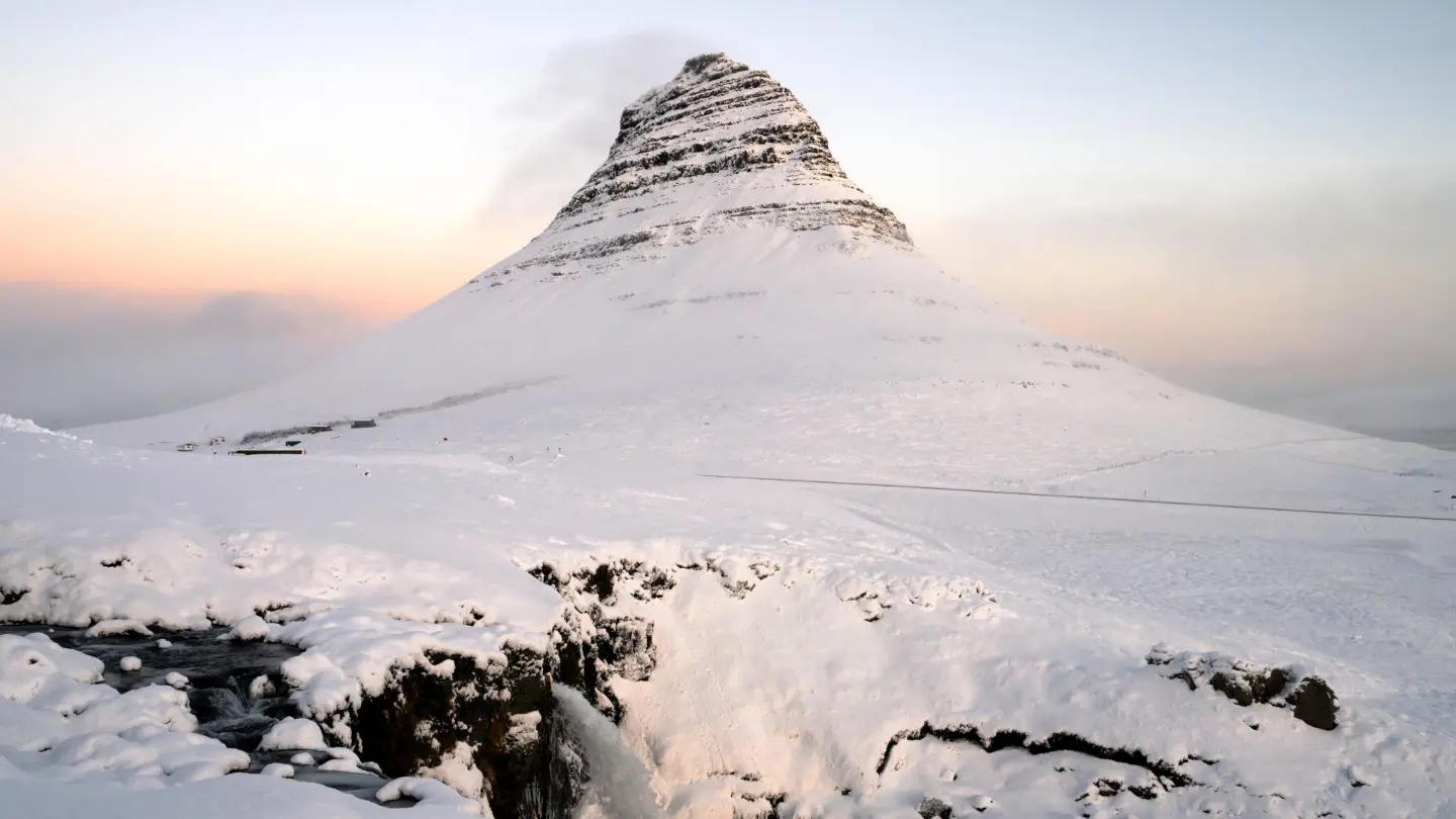 A snow covered mountain with a waterfall, under sunset light