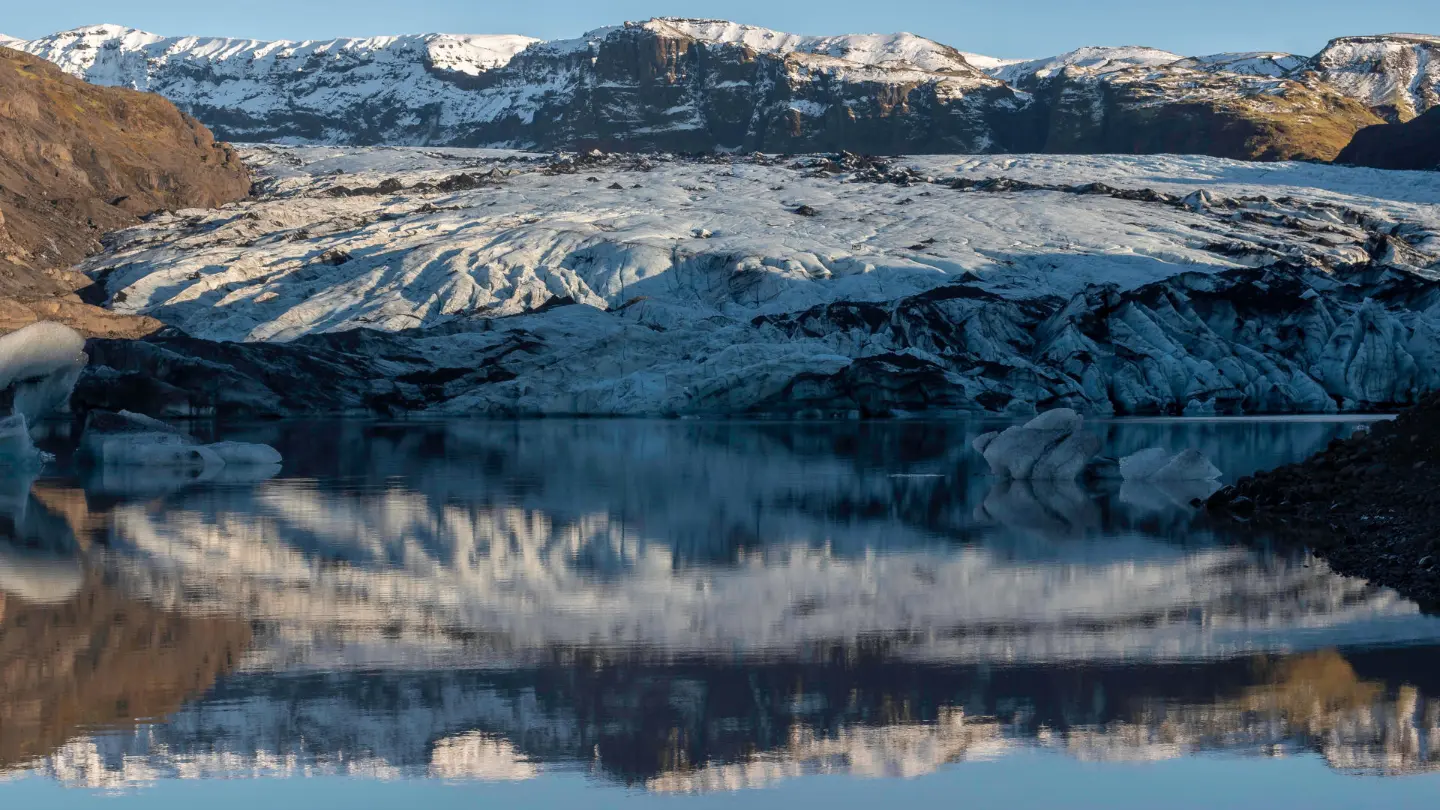 The end of a glacier is mirroring on the still water of a glacier lake