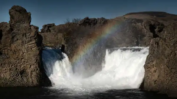 A double waterfall falls into a lake, while a rainbow shines above