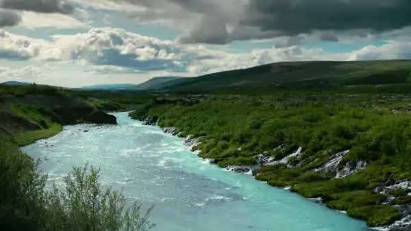 An immense blue river seems to be filled by dozens of waterfalls coming from the vegetation