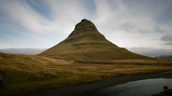 A stand-alone, conic, green mountain under blue sky