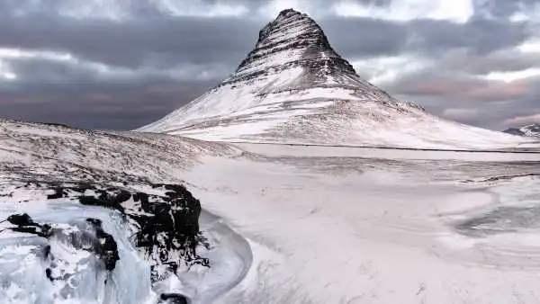 In a white-out winter landscape, we can see two frozen waterfalls in the foreground and a triangular mountain in the back