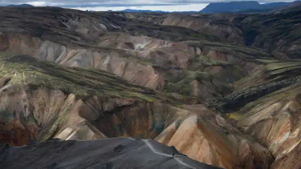 Hiking trail on black sand, with hundreds of colourful mountains in the background