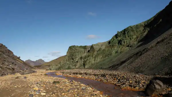 Green mountain on the side of a brown river