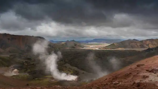 Red mountains in the foreground, with fumarolles in the back