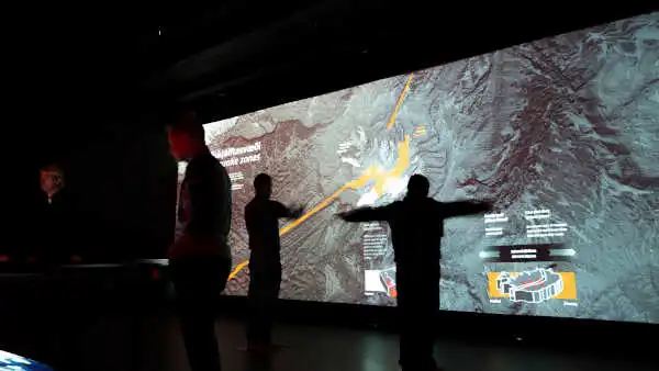 People are playing with an immense interactive screen displaying information about volcanoes and tectonic plates