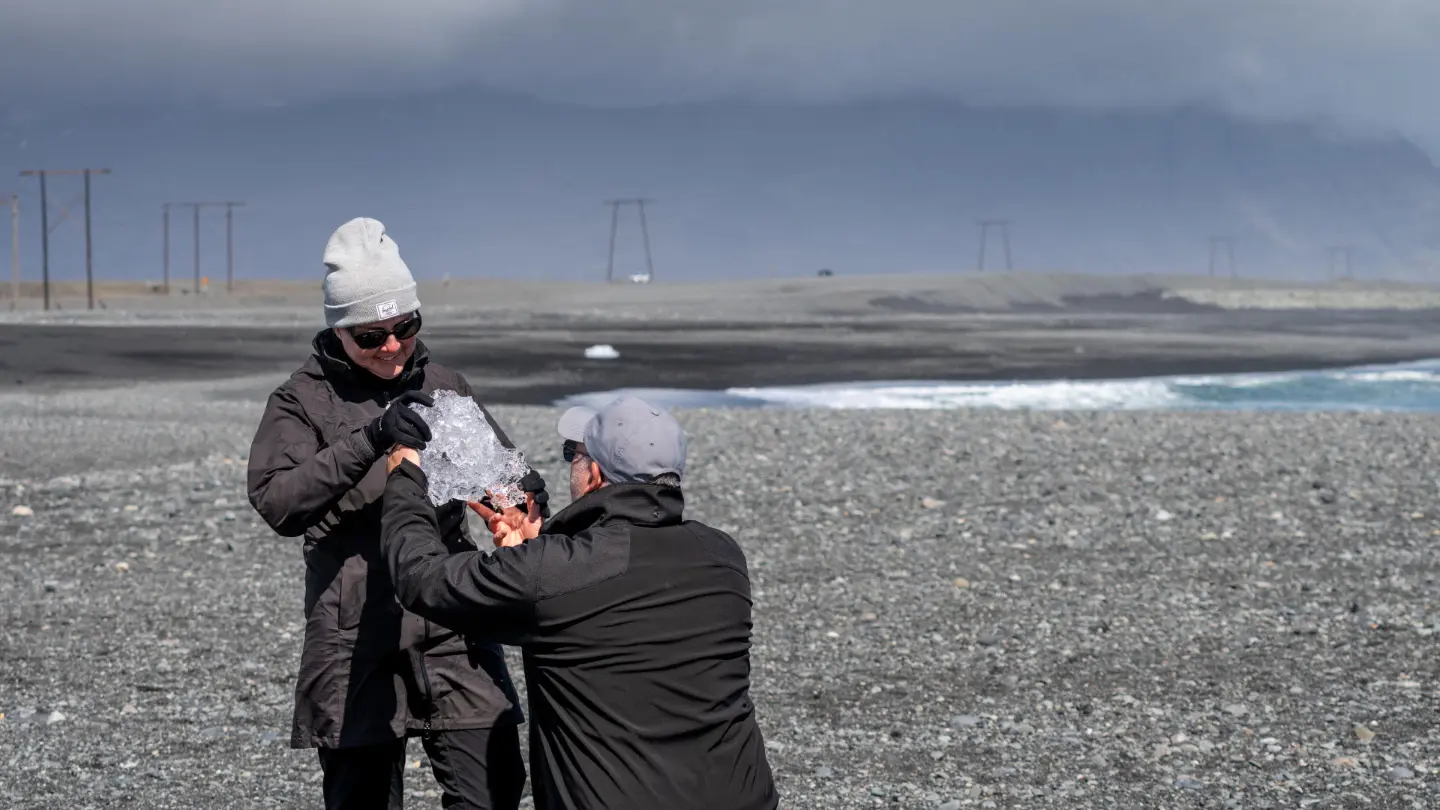 A man on his knee fakes proposing while handing his wife a piece of ice