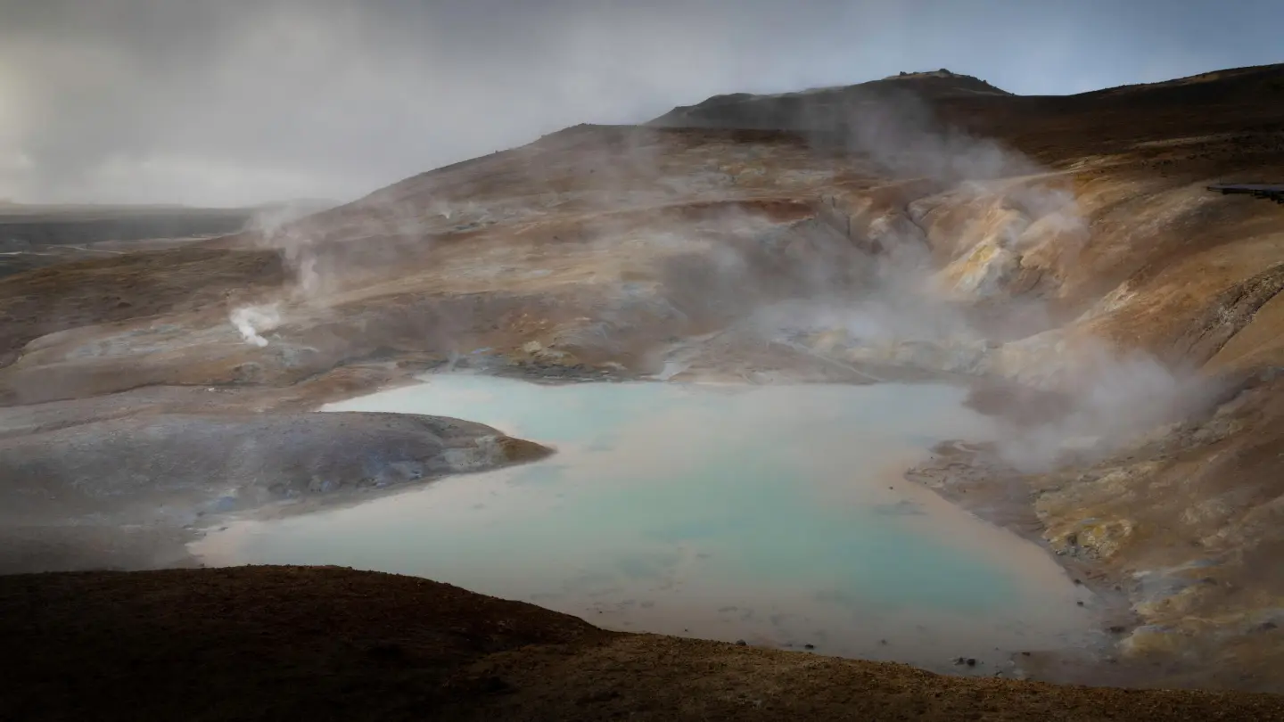 Steam coming from turquoise blue waters before orange mountains