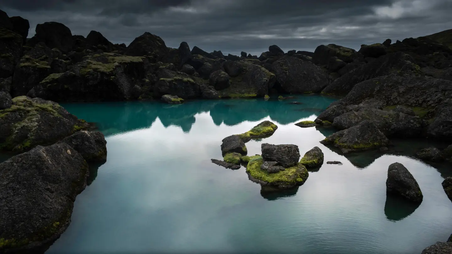 Turquoise blue natural pool between mossy dark rocks