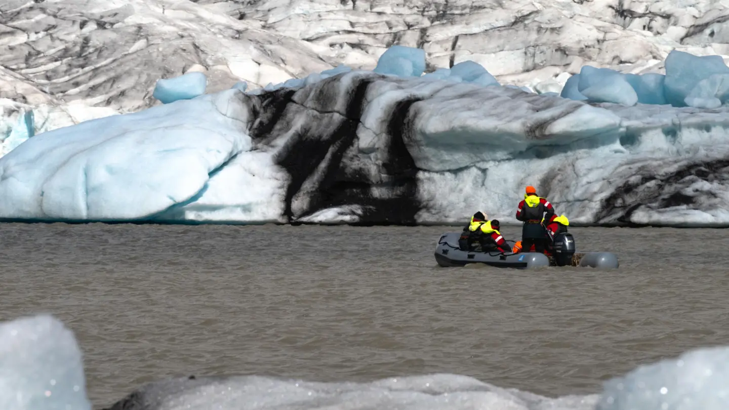 A zodiac boat with people inside is reaching to icebergs