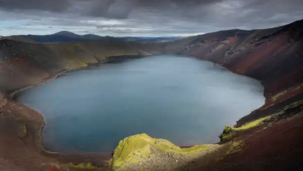 A beautiful blue crater lake, surrounded by red mountains and green moss