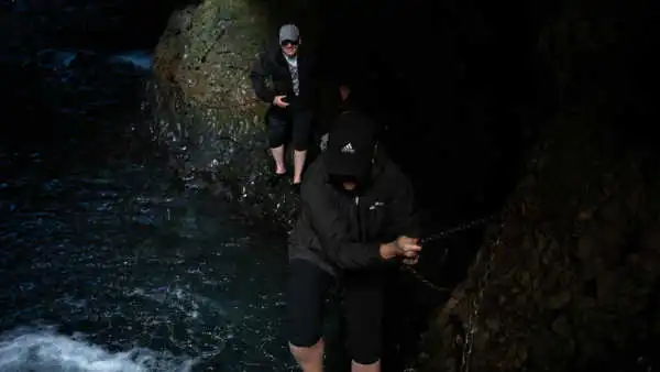 People are clinging on chains to find their way inside a cave along a river