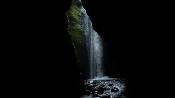 In a dark canyon, a waterfall can be seen at the end